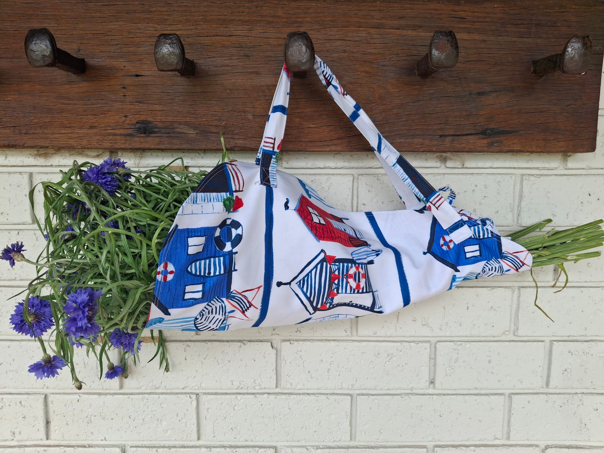 Fabric with house pattern draped over a wooden coat rack against a white brick wall.