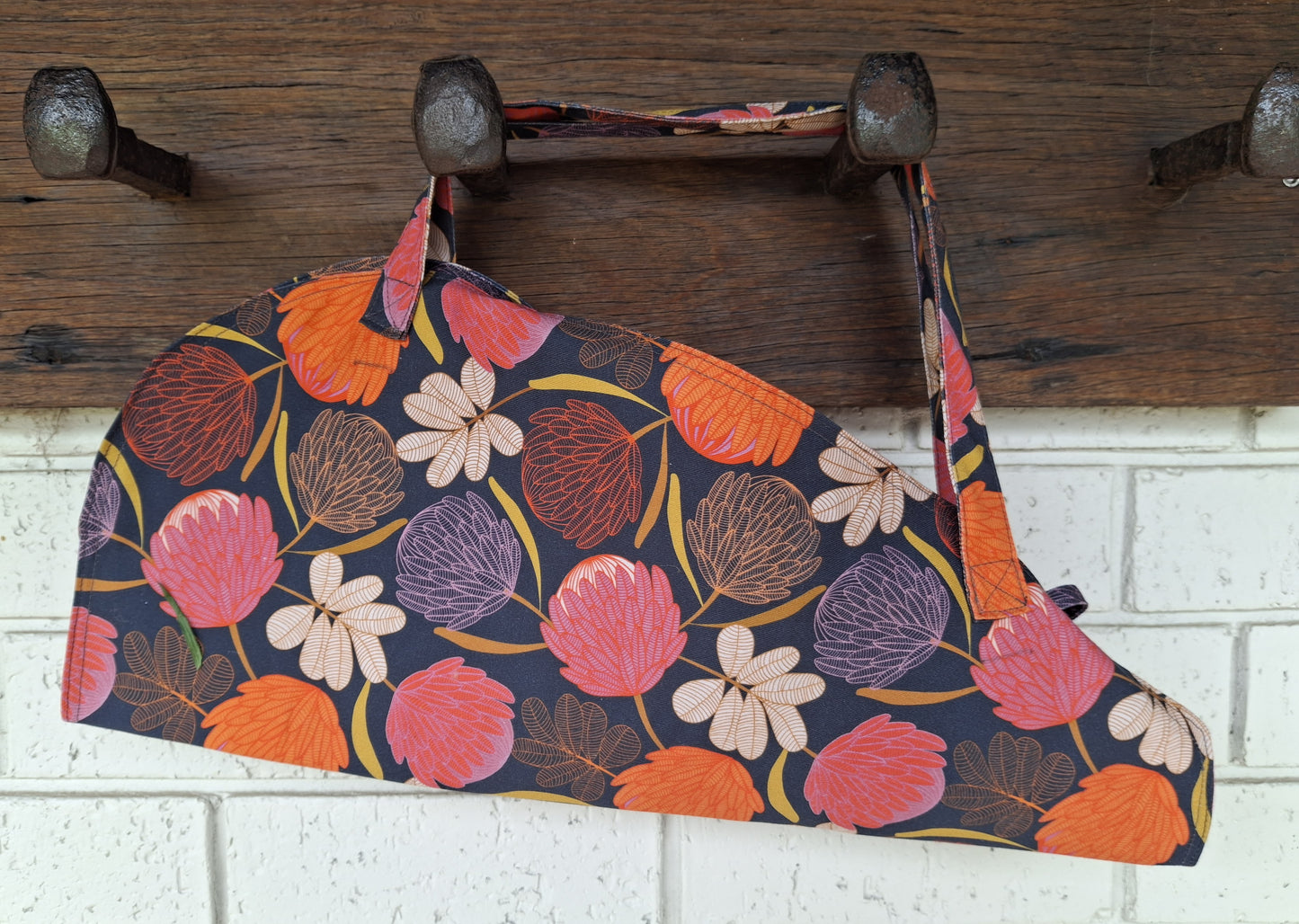Floral-patterned bag hanging on a wooden hook against a white brick wall.