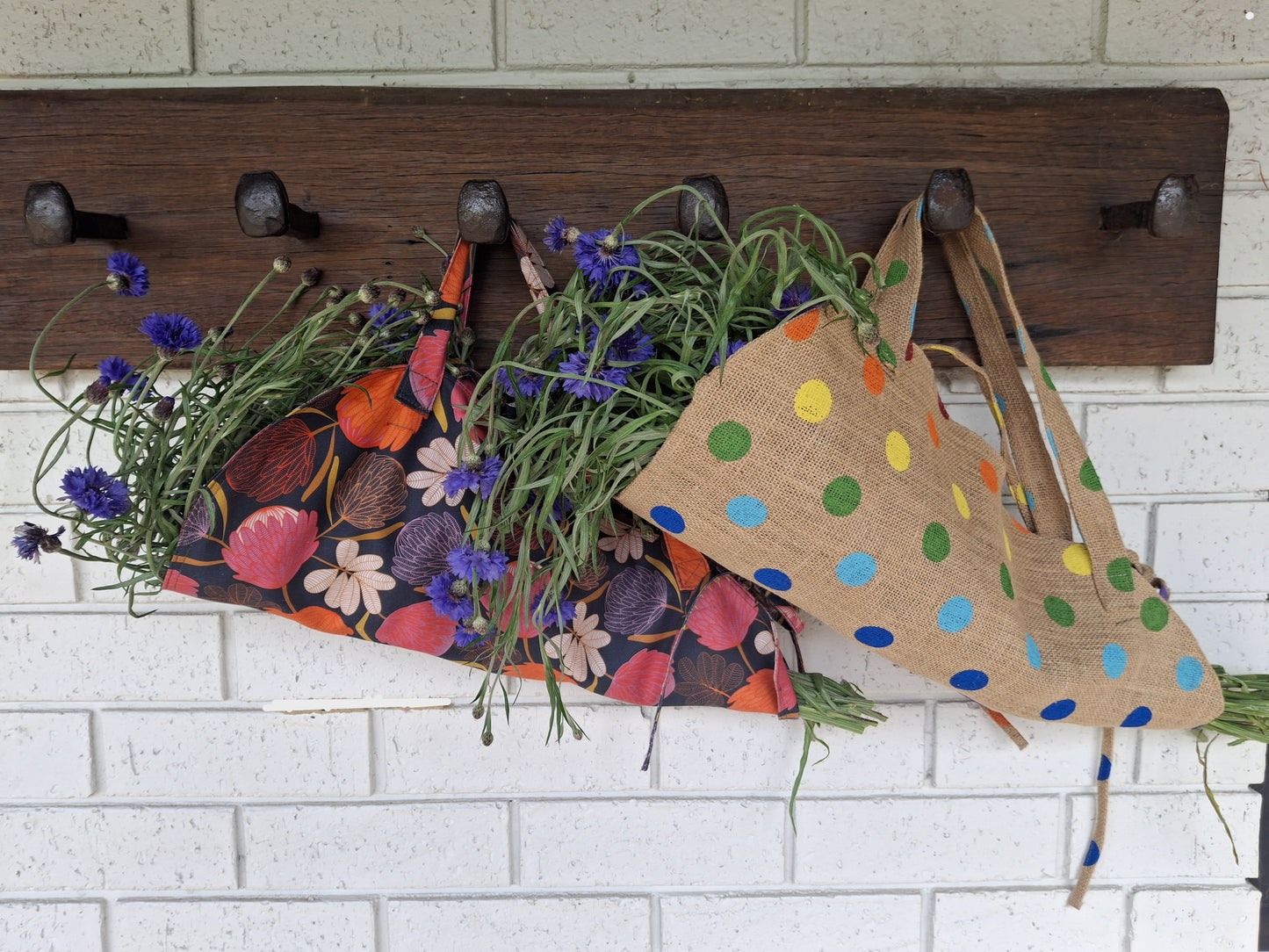 Wooden wall hook with floral bag, greenery, and polka dot bag on a white brick wall.